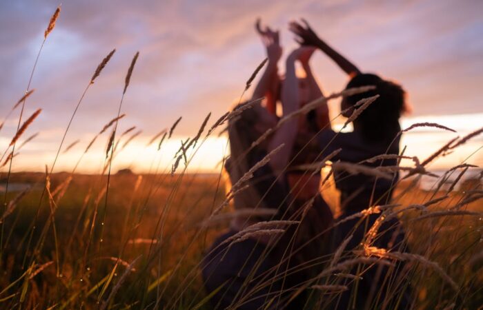 Safe period products: Three silhouetted figures playfully reach towards the sky amidst tall grass, illuminated by a vibrant sunset.