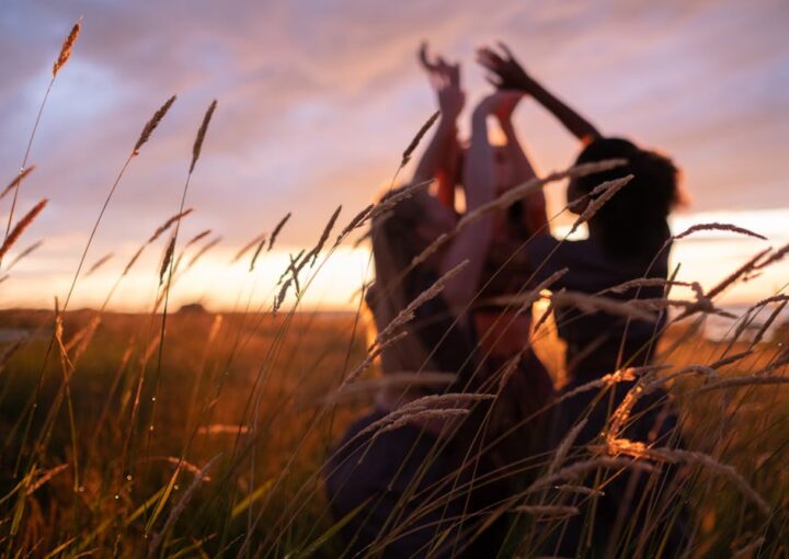 Safe period products: Three silhouetted figures playfully reach towards the sky amidst tall grass, illuminated by a vibrant sunset.