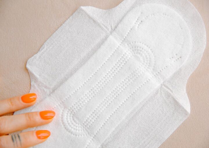 Organic pads in the UAE; A close-up of a white sanitary pad on a light surface, with a hand featuring bright orange nails gently resting beside it.