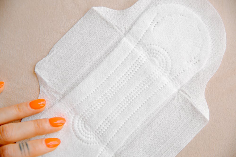 Organic pads in the UAE; A close-up of a white sanitary pad on a light surface, with a hand featuring bright orange nails gently resting beside it.