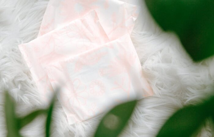Three sanitary pads with a delicate floral pattern arranged on soft, white fur, partially framed by green leaves.
