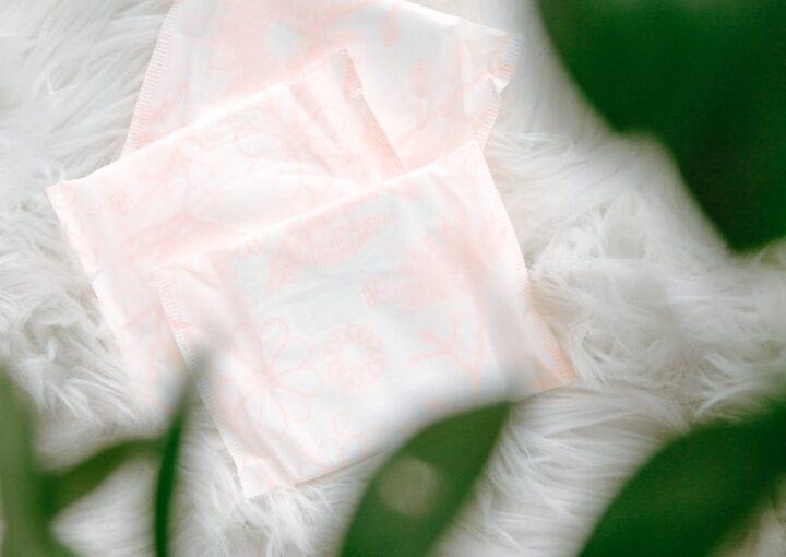Three sanitary pads with a delicate floral pattern arranged on soft, white fur, partially framed by green leaves.