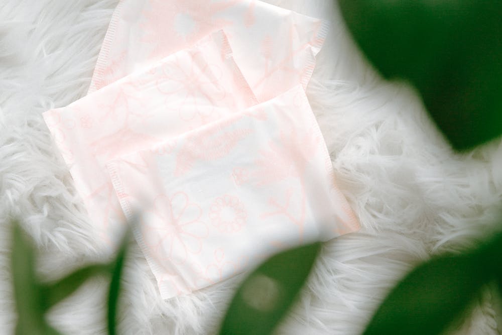 Three sanitary pads with a delicate floral pattern arranged on soft, white fur, partially framed by green leaves.